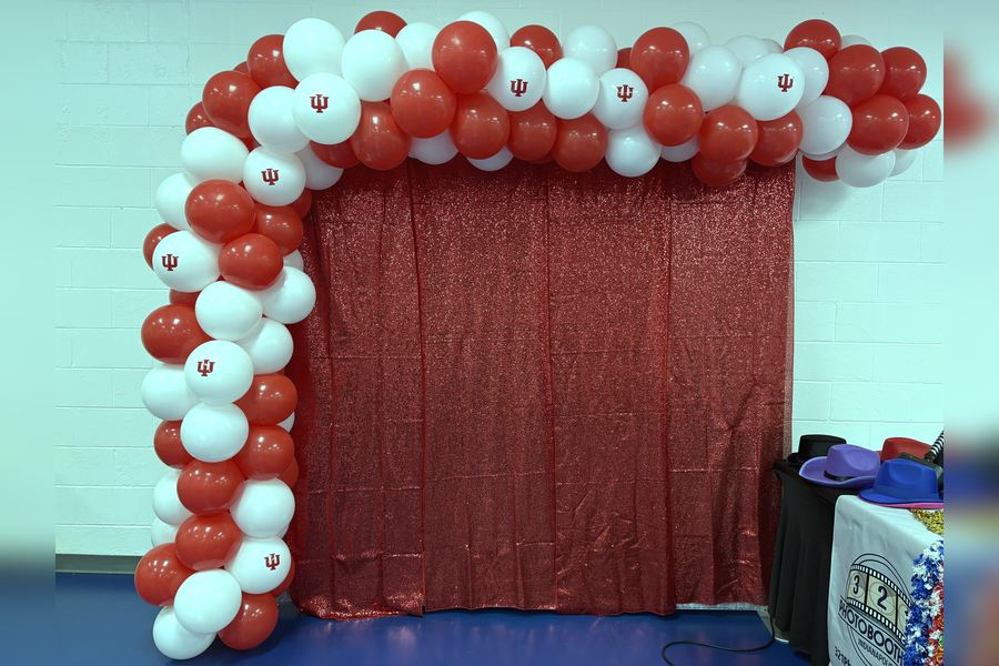 Red and white balloon arch, IU crimson, framing a red sequin backdrop in a school gym.